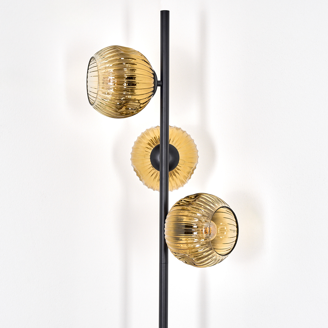 Eine moderne Lampe mit schwarzem Pfosten und drei goldenen Glasschirmen. Die Schirme sind rund und haben eine gerippte Struktur.