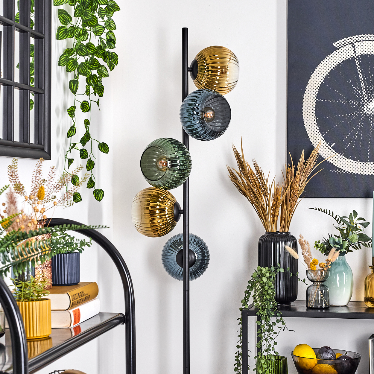 Ein modernes Interieur mit einer Stehlampe mit Kugelleuchten. Regal mit Pflanzen, Büchern und Vasen. Kunstwerk eines Fahrradrads an der Wand.