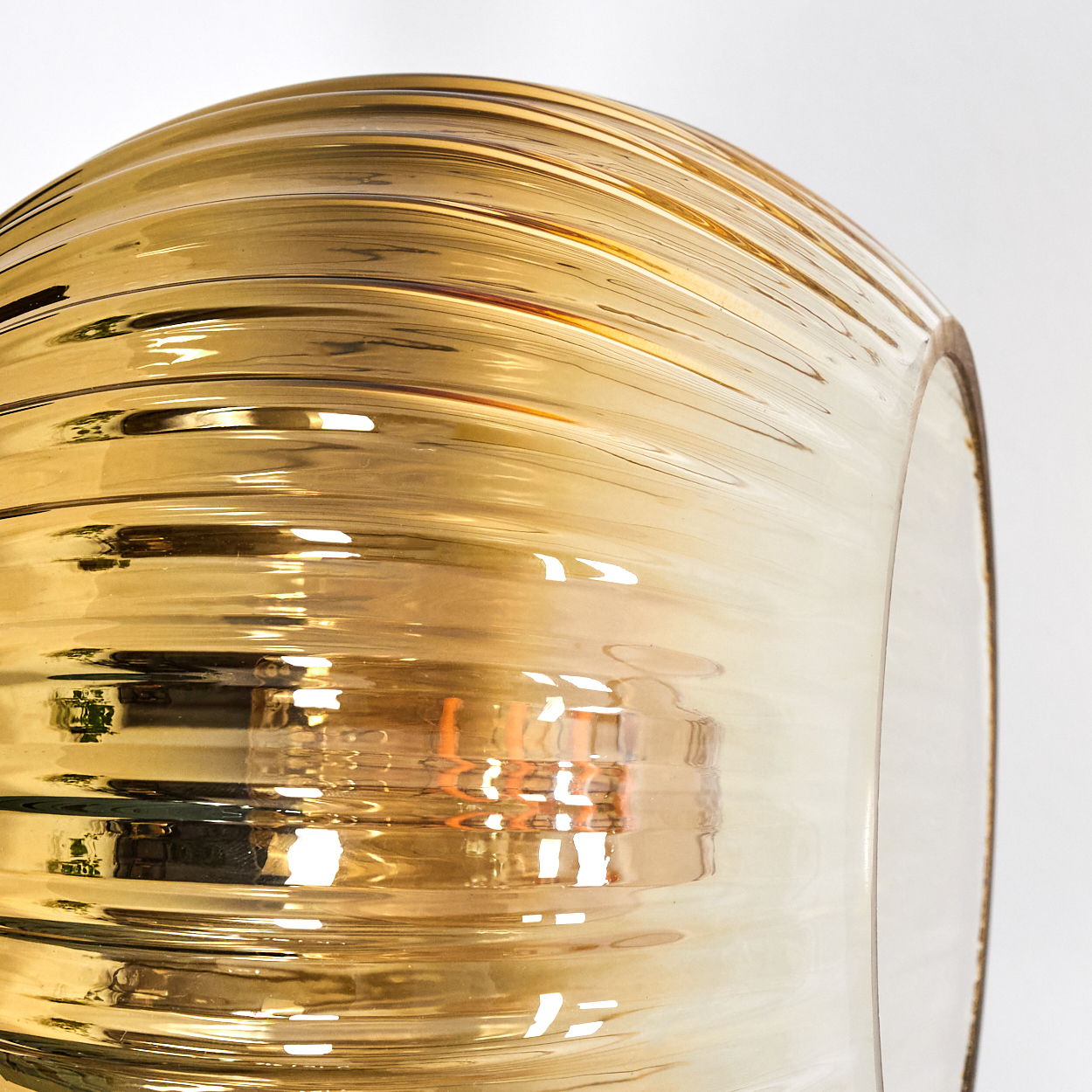 Nahaufnahme eines Glasobjekts. Das Objekt hat einen goldenen Farbton mit gerippter Textur. Es ist vor einem weißen Hintergrund platziert und reflektiert Licht.