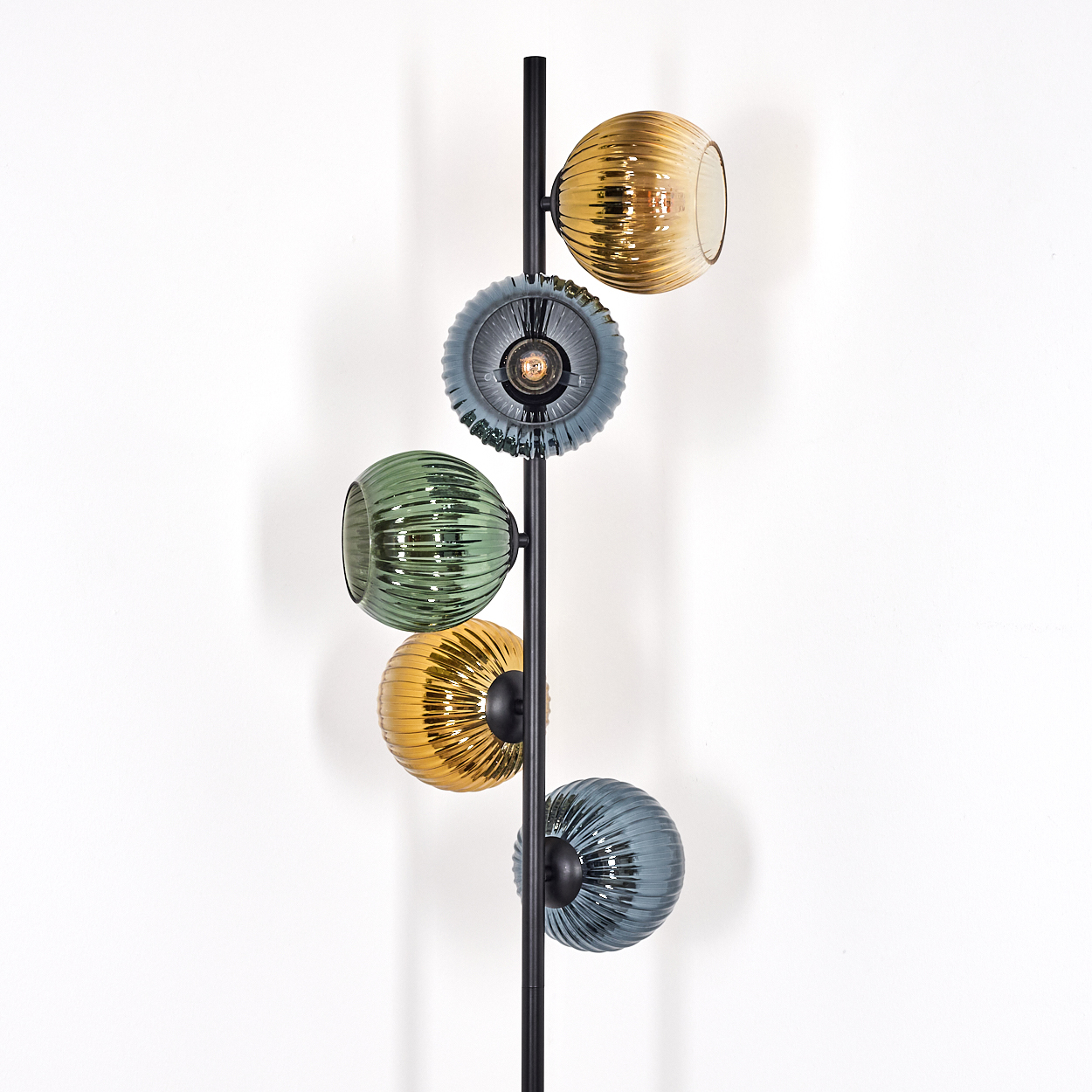 Eine moderne Stehlampe mit fünf farbigen, gerippten Glas-Kugel-Schirmen. Die Lampe hat eine schwarze Metallsäule vor einer weißen Wand.