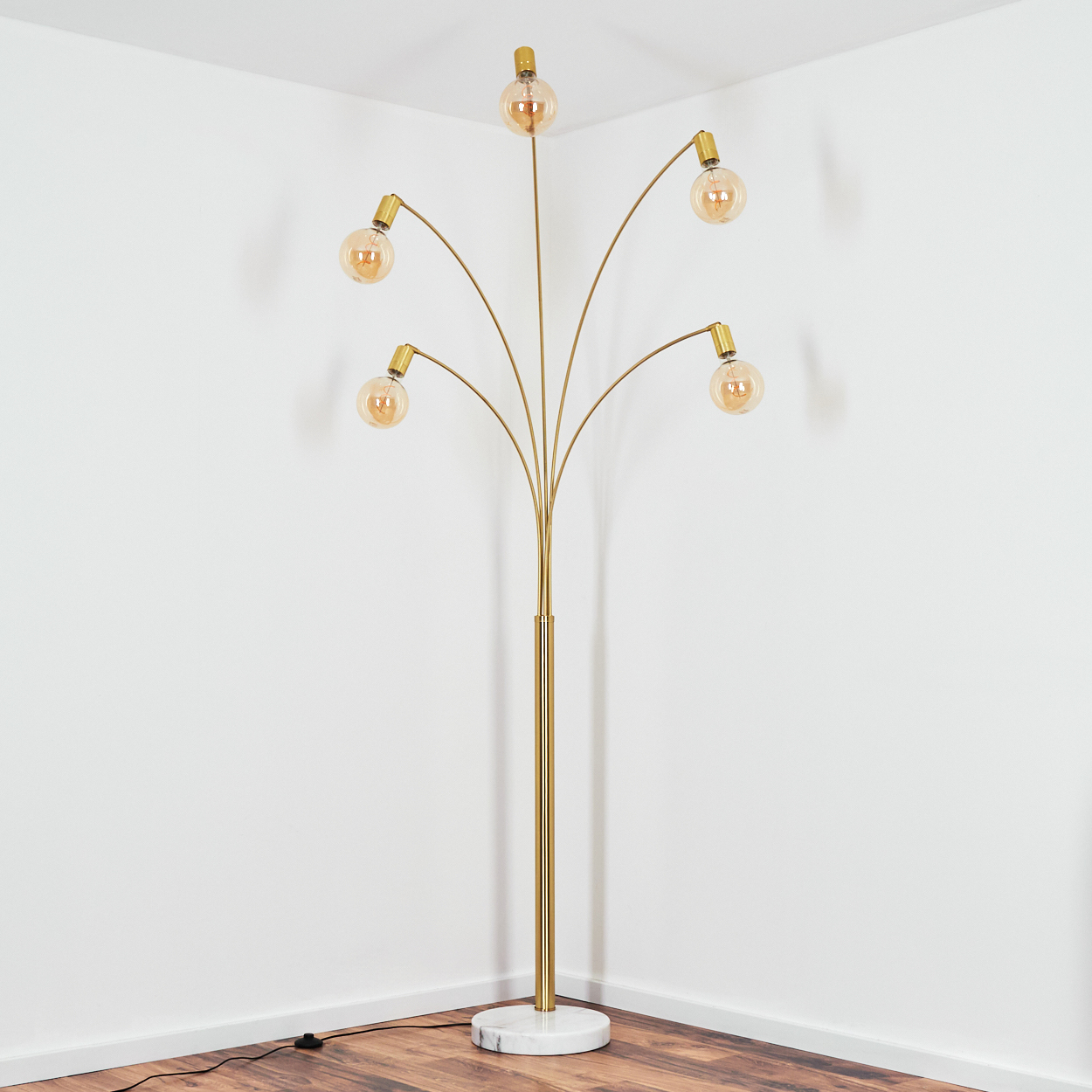 Eine goldene Stehlampe mit sechs Glühbirnen steht in einer Ecke. Sie hat einen Marmorsockel, und der Boden ist aus Holz. Weiße Wände bilden den Hintergrund.