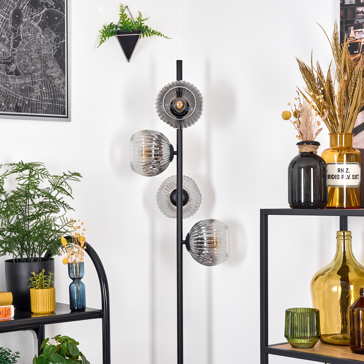 Ein modernes Wohnzimmer mit schwarzer Stehlampe, Vasen mit Pflanzen, einer Karte und einem Regal mit Flaschen.