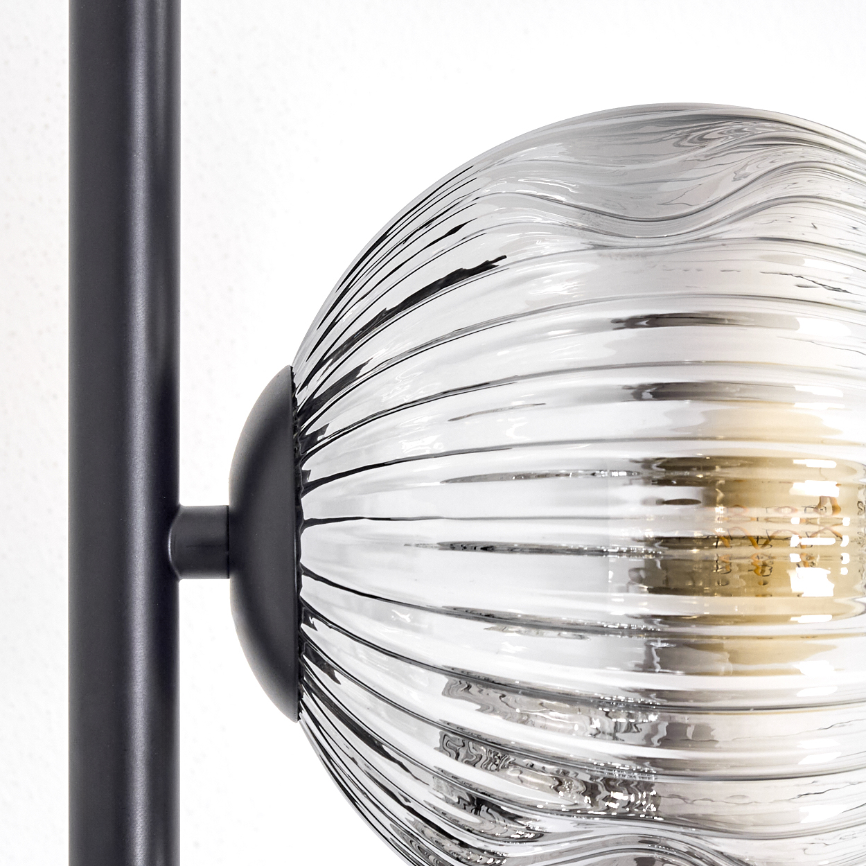Nahaufnahme einer Lampe mit gerippter Glaskugel und schwarzem Metallträger. Der Hintergrund ist weiß.
