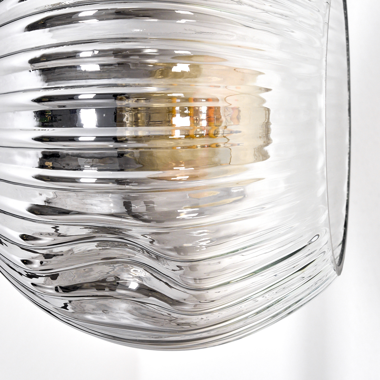 Nahaufnahme eines transparenten Glasobjekts mit welliger Textur. Licht reflektiert, erzeugt Leuchteffekt. Weißer Hintergrund.