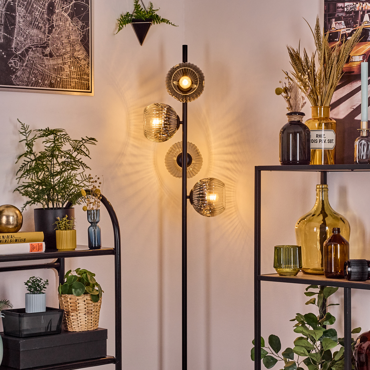 Ein Raum mit einer modernen Stehlampe, Regalen mit Pflanzen und Dekoration und einer Karte an der Wand. Weiches Licht.