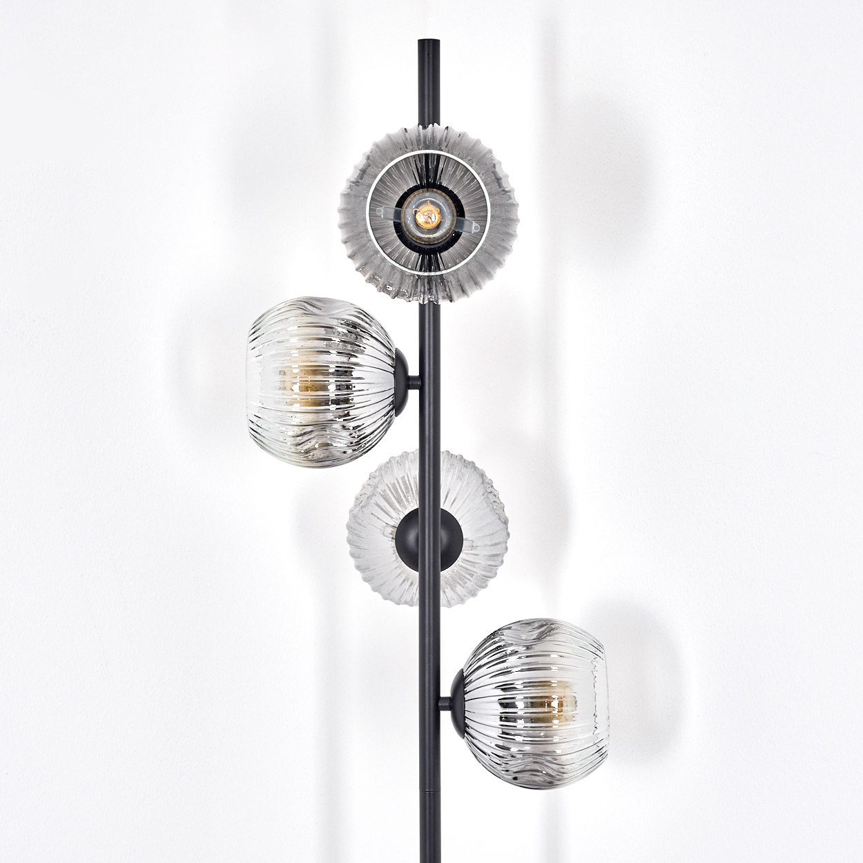 Eine moderne schwarze Lampe mit drei Leuchten. Zwei sind kugelförmig, eine ist kreisförmig. Alle haben ein geripptes Glasdesign und sind beleuchtet.