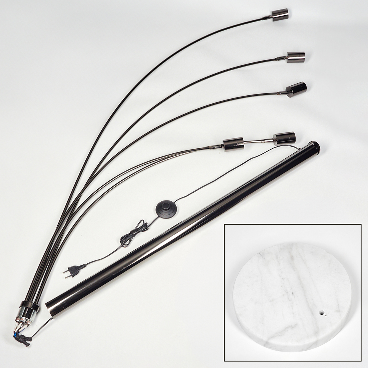 Zerlegte schwarze Stehlampe auf Weiß. Sie hat einen Marmorsockel, gebogene Arme und zylindrische Lampenköpfe. Teile sind verstreut.