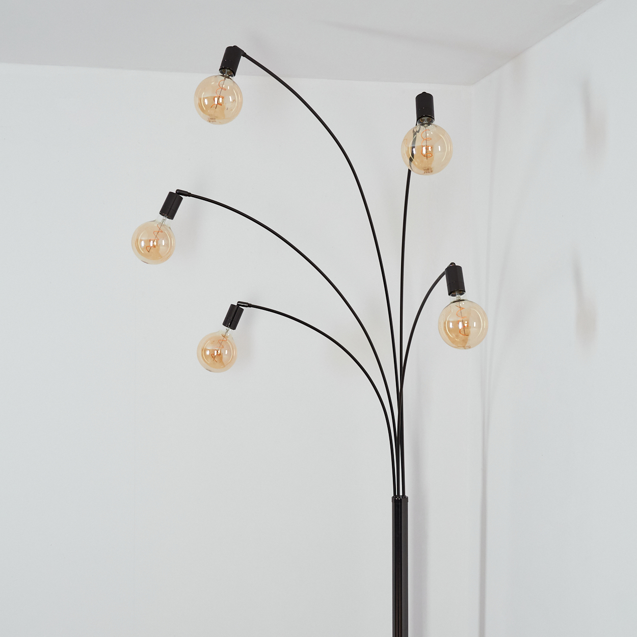 Eine moderne schwarze Stehlampe mit fünf gebogenen Armen, die jeweils eine runde, bernsteinfarbene Glühbirne halten, vor einer weißen Wand.