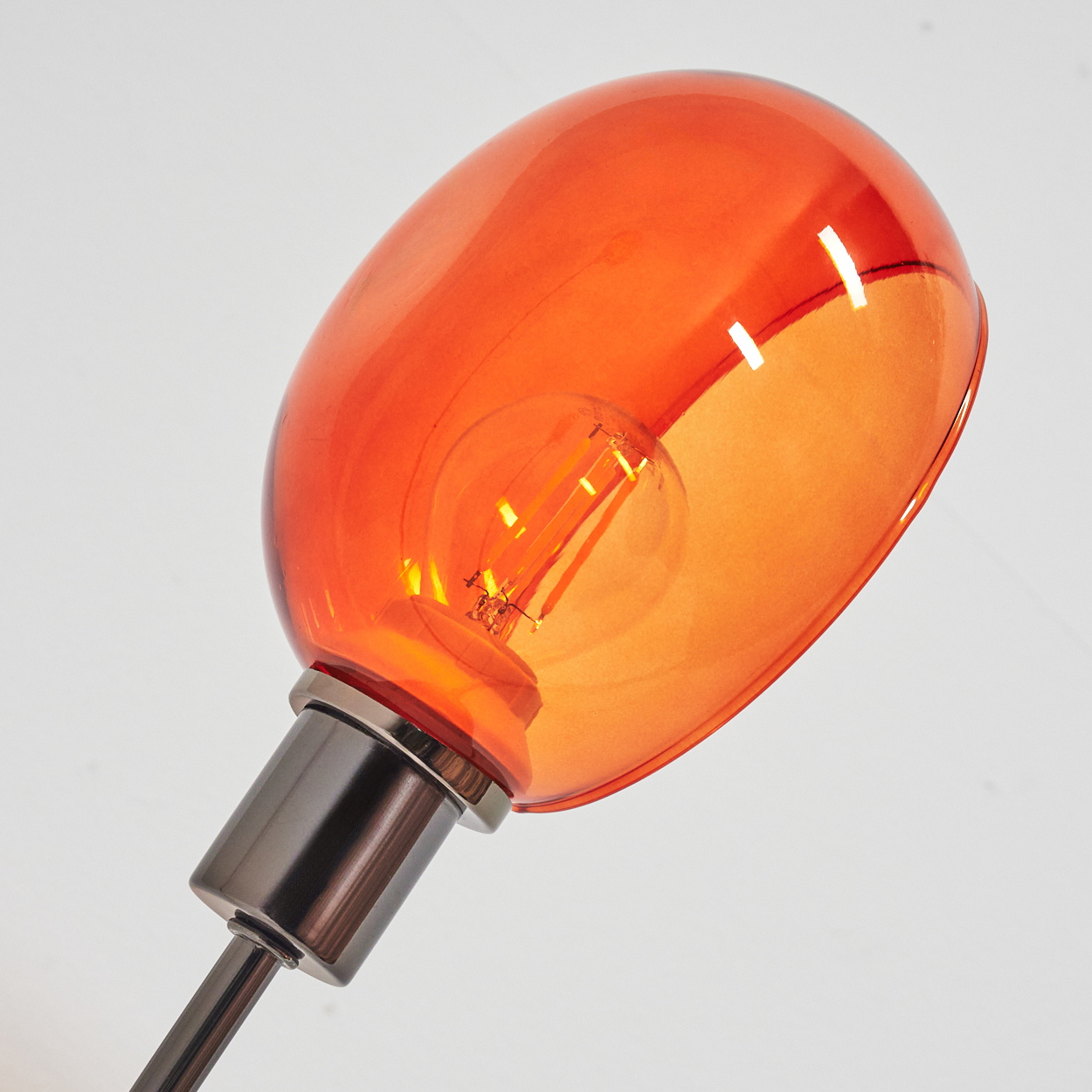 Nahaufnahme einer Lampe mit orangefarbenem Glasschirm und sichtbarer Glühbirne. Der Sockel und der Stiel sind metallisch.