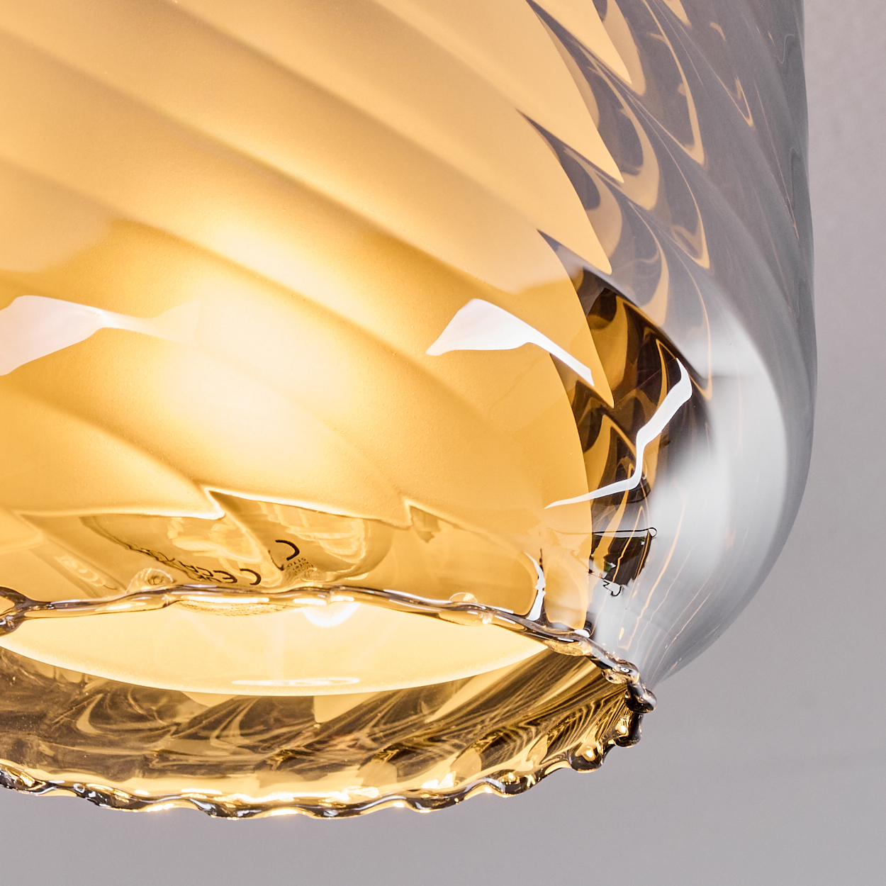 Nahaufnahme einer Glasleuchte, bernsteinfarben, mit gewelltem Design. Das Licht ist an, und der Hintergrund ist weiß.