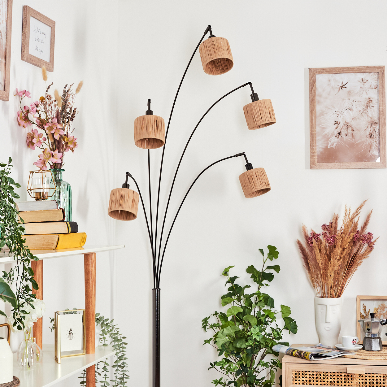 Ein modernes Wohnzimmer mit einer schwarzen Bogenlampe, Pflanzen, einem Regal mit Büchern und Bildern an einer weißen Wand.