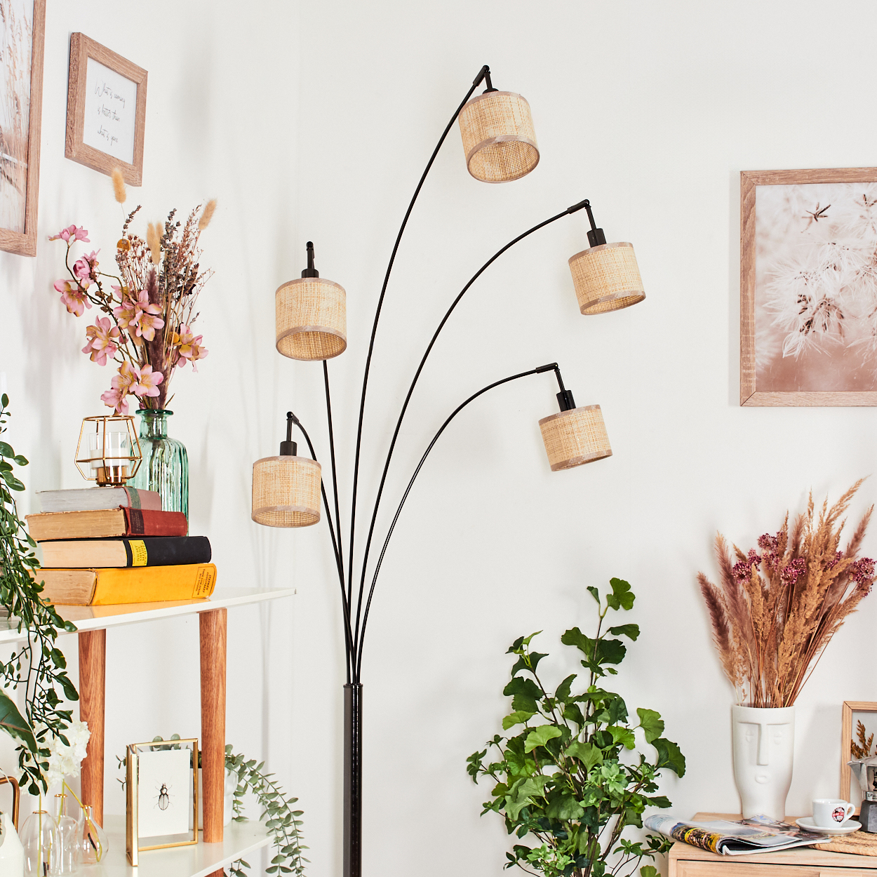 Ein modernes Wohnzimmer mit schwarzer Stehlampe, gewebten Lampenschirmen, Pflanzen, Büchern und gerahmter Kunst an weißen Wänden.