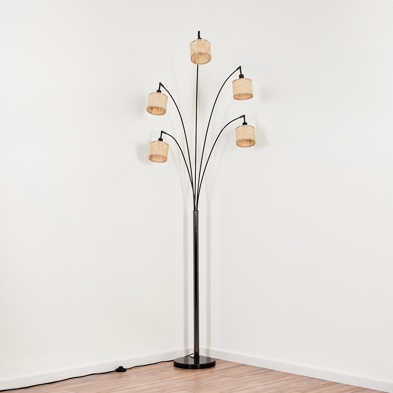Eine Stehlampe mit fünf Lampenschirmen. Die Lampe ist schwarz mit beigefarbenen Schirmen, in einer Ecke mit weißen Wänden und Holzboden platziert.