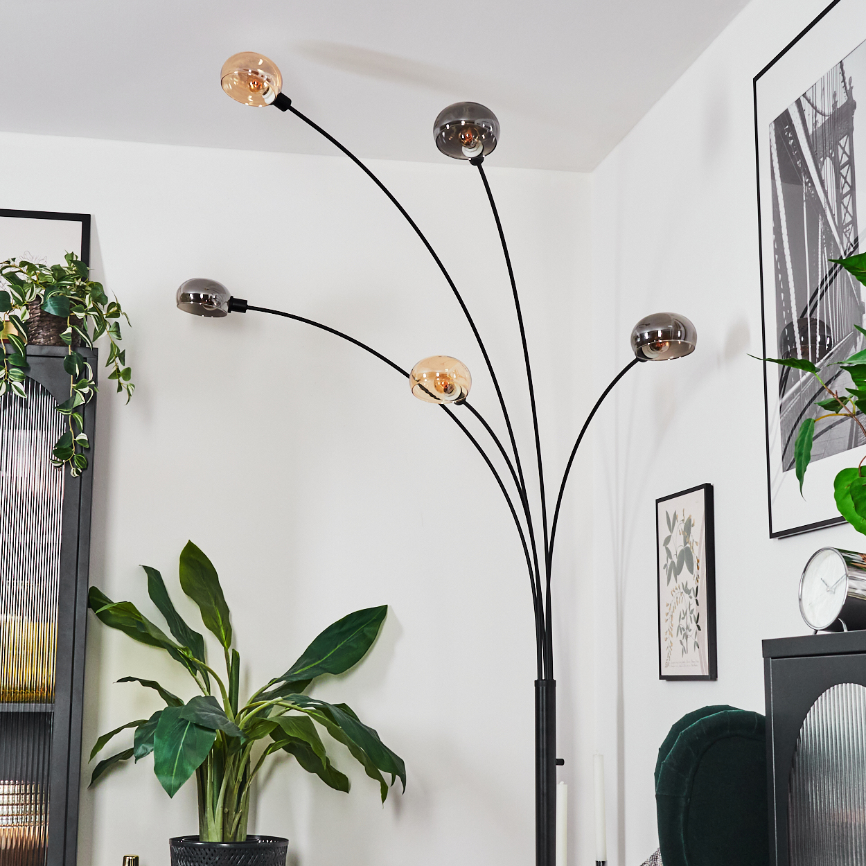 Eine moderne Stehlampe mit fünf Glühbirnen. Im Raum gibt es eine Pflanze, ein Bild, einen schwarzen Schrank und einen grünen Stuhl.