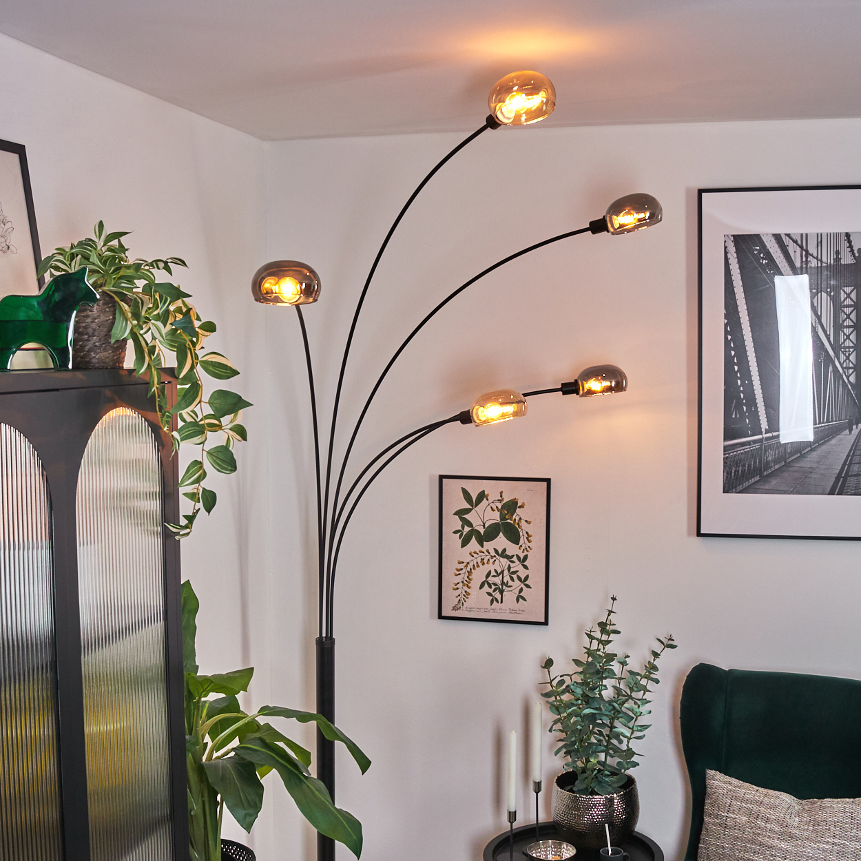 Ein modernes Wohnzimmer mit schwarzer Stehlampe, Pflanzen und gerahmter Kunst. Die Lampe hat fünf Glühbirnen, die den Raum beleuchten.