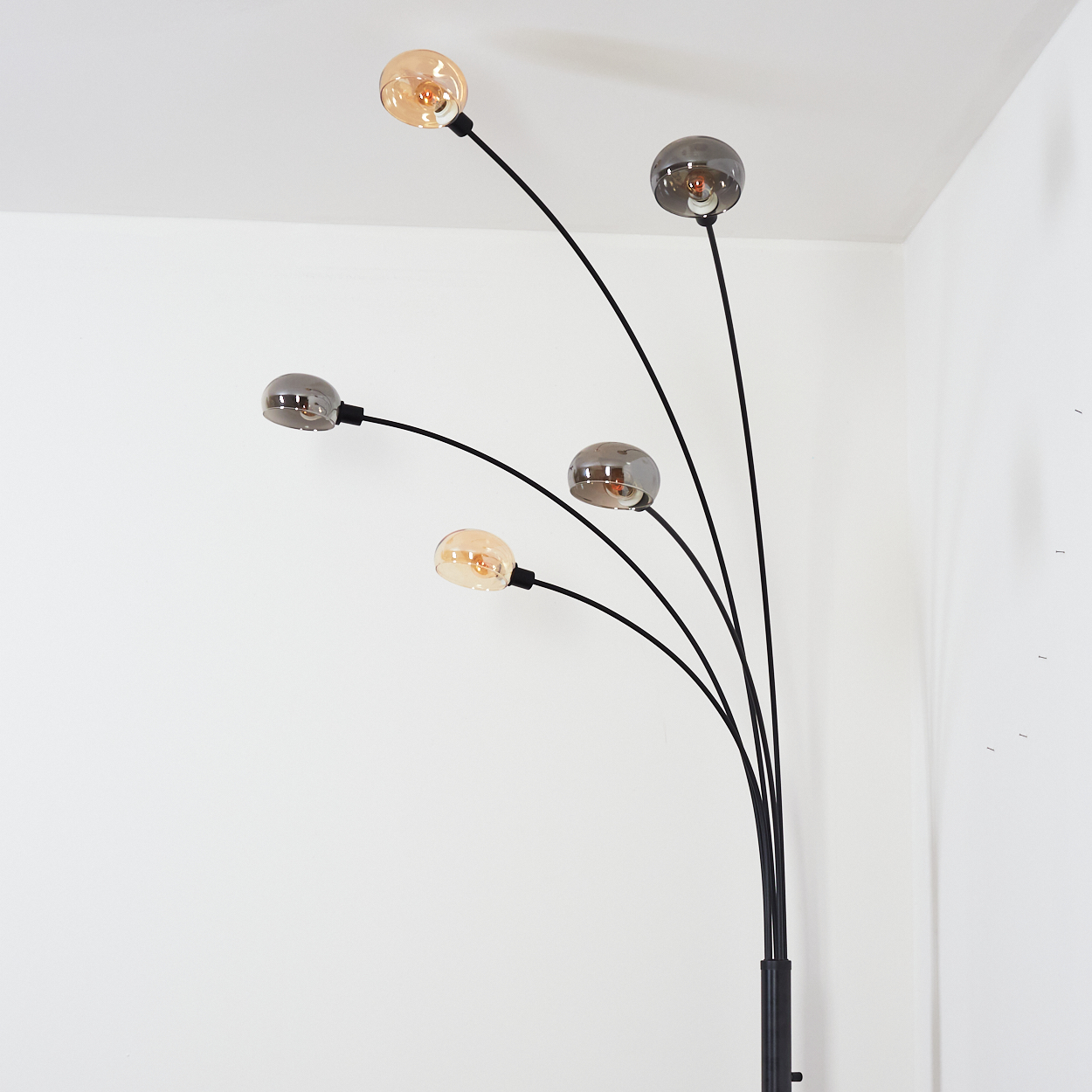 Eine moderne Stehlampe mit fünf Glühbirnen. Die Glühbirnen sind rund und in verschiedenen Farbtönen. Die Lampe ist schwarz und steht in einem weißen Raum.