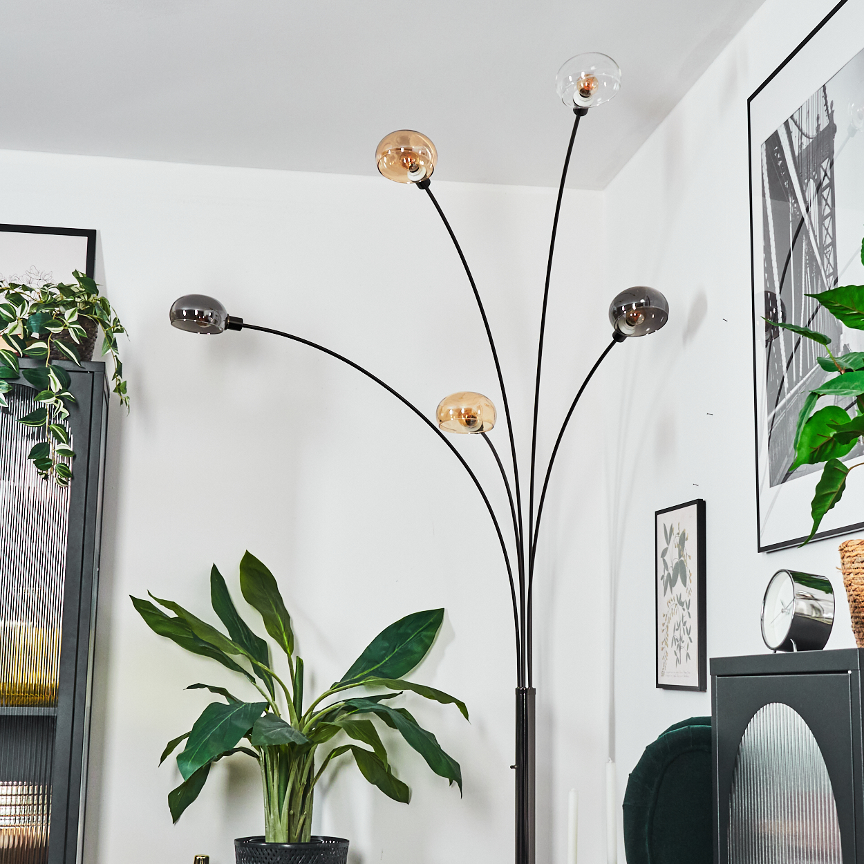 Eine moderne Stehlampe mit Glaskugelschirmen steht in der Nähe von Pflanzen und gerahmter Kunst. Die Lampe hat ein schwarzes Metallgestell.
