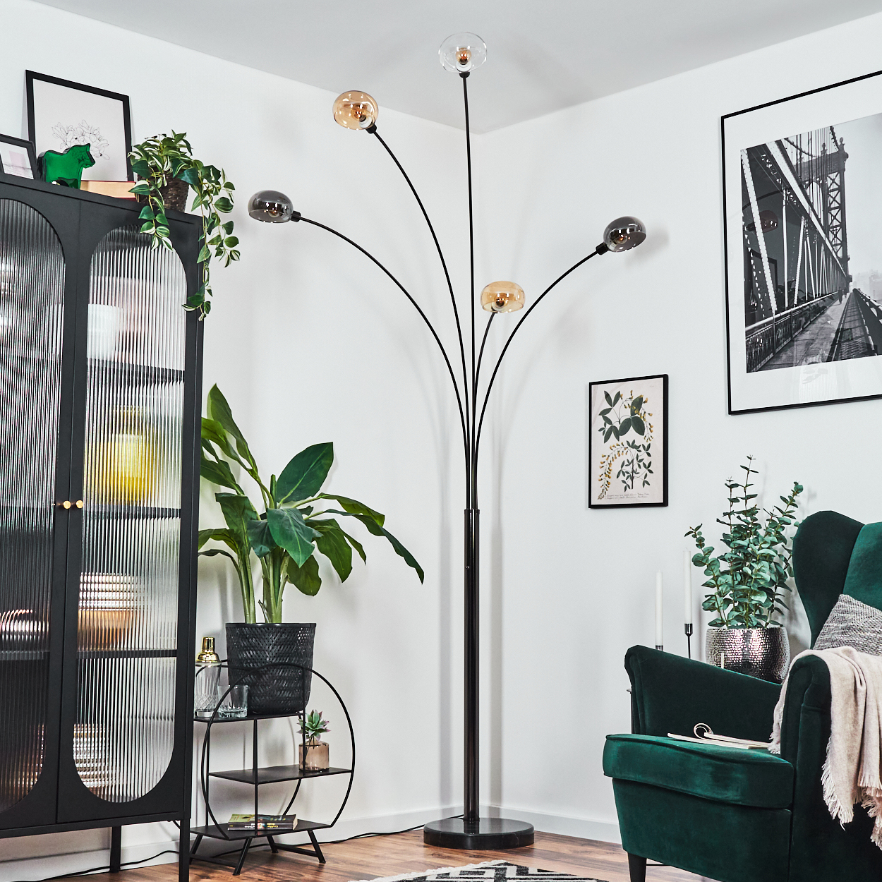 Ein modernes Wohnzimmer mit schwarzer Stehlampe, grünem Sessel und schwarzem Schrank. Pflanzen und gerahmte Kunstwerke sind vorhanden.