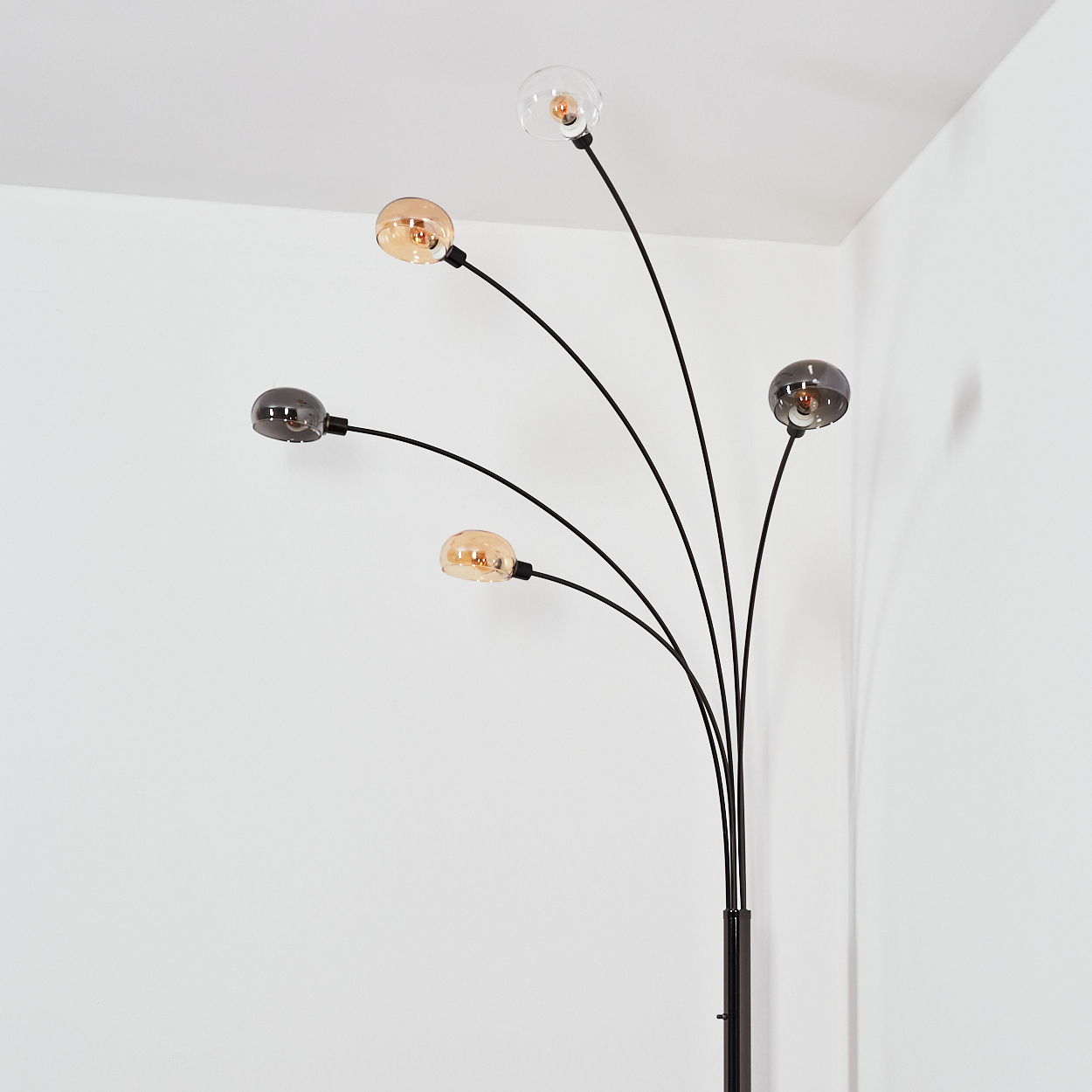 Eine moderne schwarze Stehlampe mit fünf gebogenen Armen, die jeweils eine kugelförmige Leuchte halten. Die Glühbirnen sind verschiedenfarbig vor einer weißen Wand.