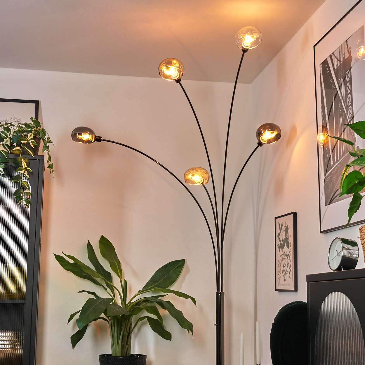 Eine moderne Stehlampe mit fünf Kugellampen. Grüne Pflanzen, ein schwarzer Schrank und gerahmte Kunst schmücken den Raum.