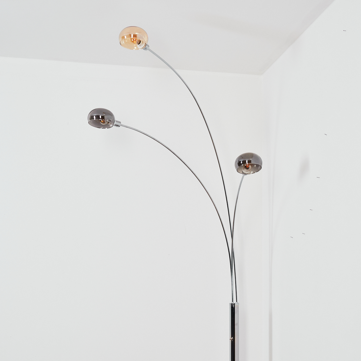 Eine moderne Stehlampe mit drei gebogenen Armen, die jeweils ein kugelförmiges Licht halten. Die Lichter sind in verschiedenen Bernstein- und Grautönen gehalten.