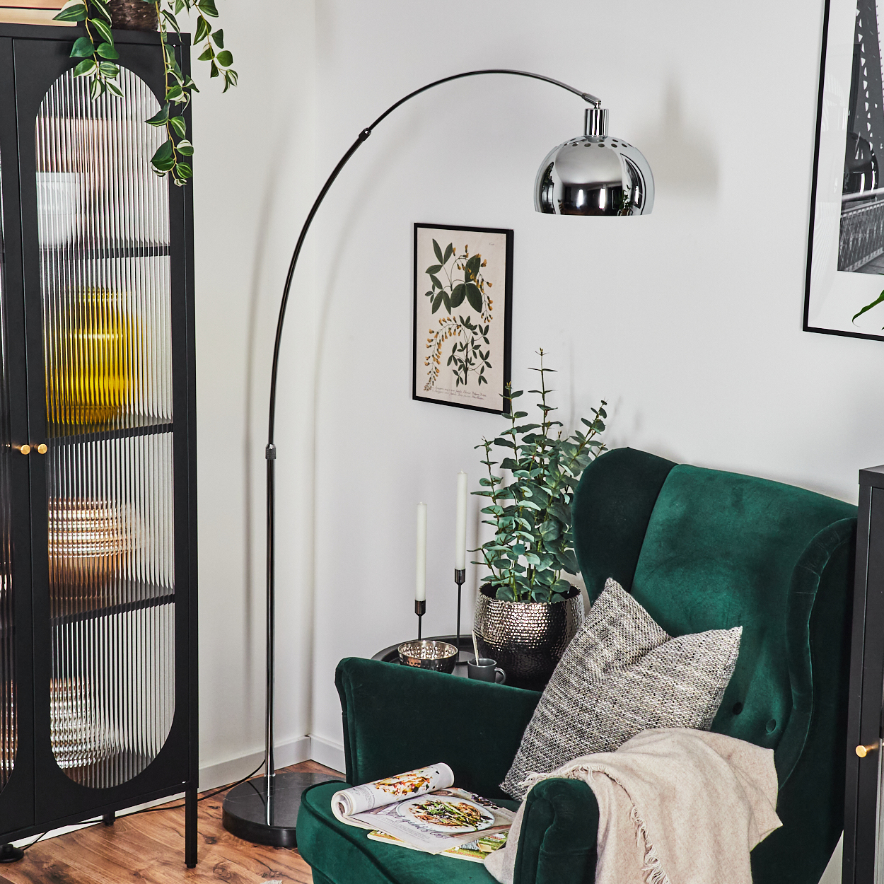 Ein modernes Wohnzimmer mit grünem Sessel, Stehlampe, schwarzem Schrank und botanischer Kunst an der Wand.