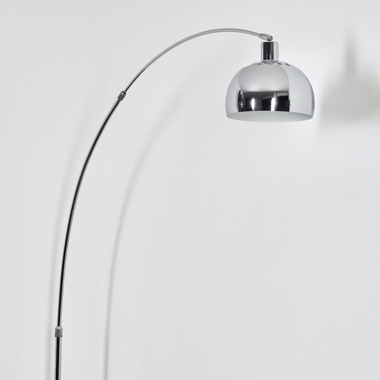 Eine verchromte Bogenstehlampe. Die Lampe hat einen kuppelförmigen Kopf und einen gebogenen Arm, der sich von einem vertikalen Sockel erstreckt.