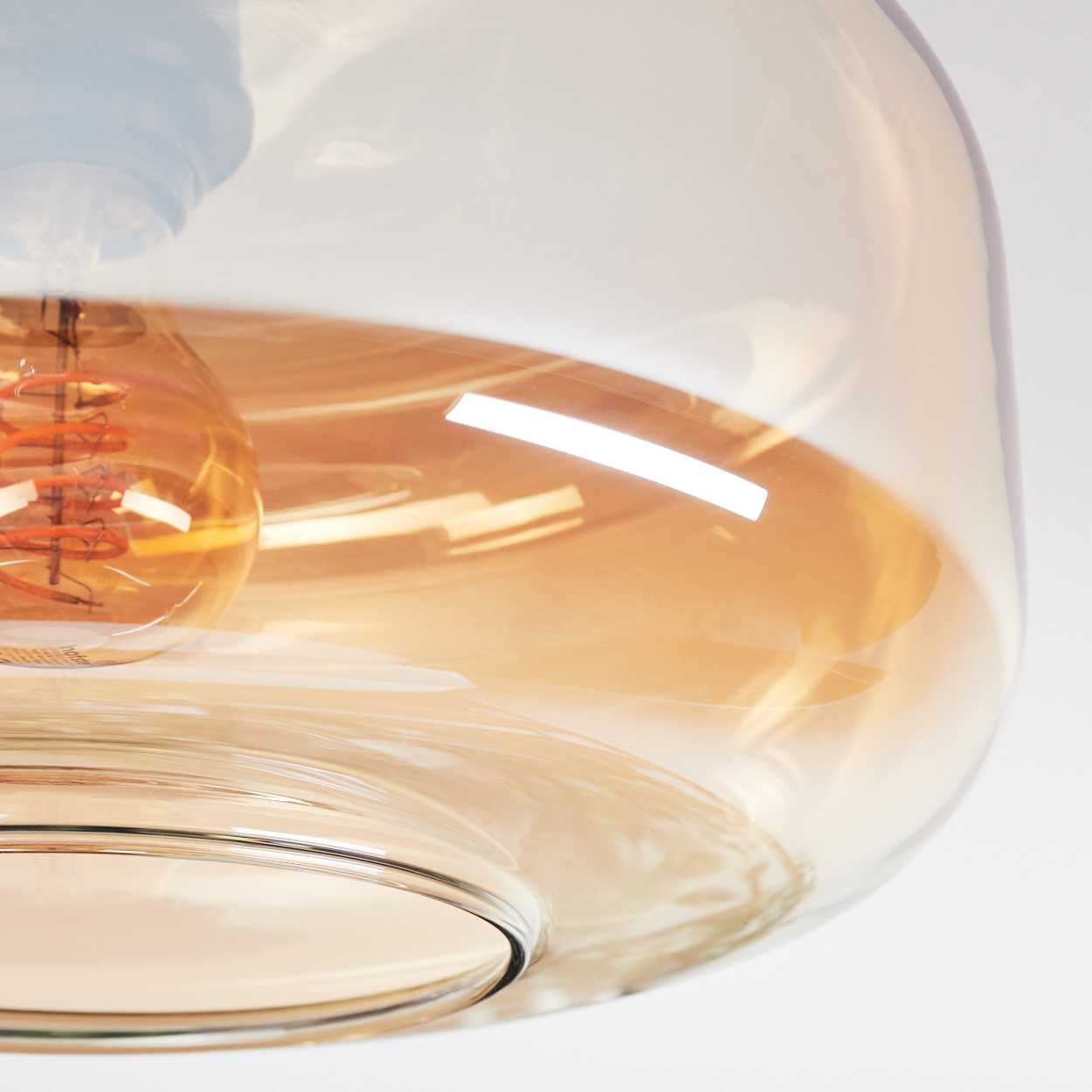 Nahaufnahme einer Leuchte mit großem, klarem Glasschirm. Im Inneren des Schirms befindet sich eine spiralförmige Glühbirne.