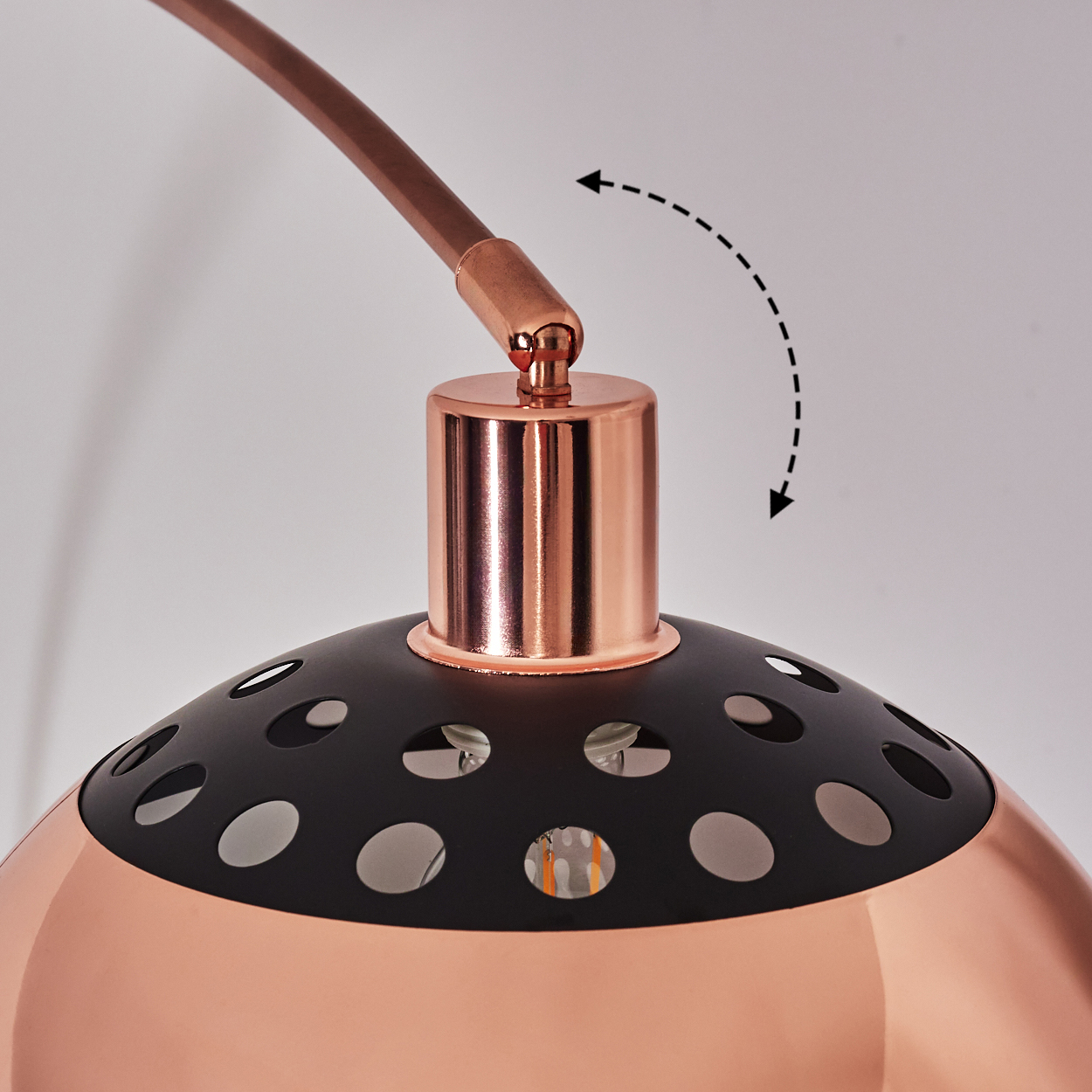 Nahaufnahme einer Kupfer- und schwarzen Lampe. Die Lampe hat einen gebogenen Arm und einen Schirm mit Löchern. Ein Pfeil zeigt die Verstellbarkeit an.
