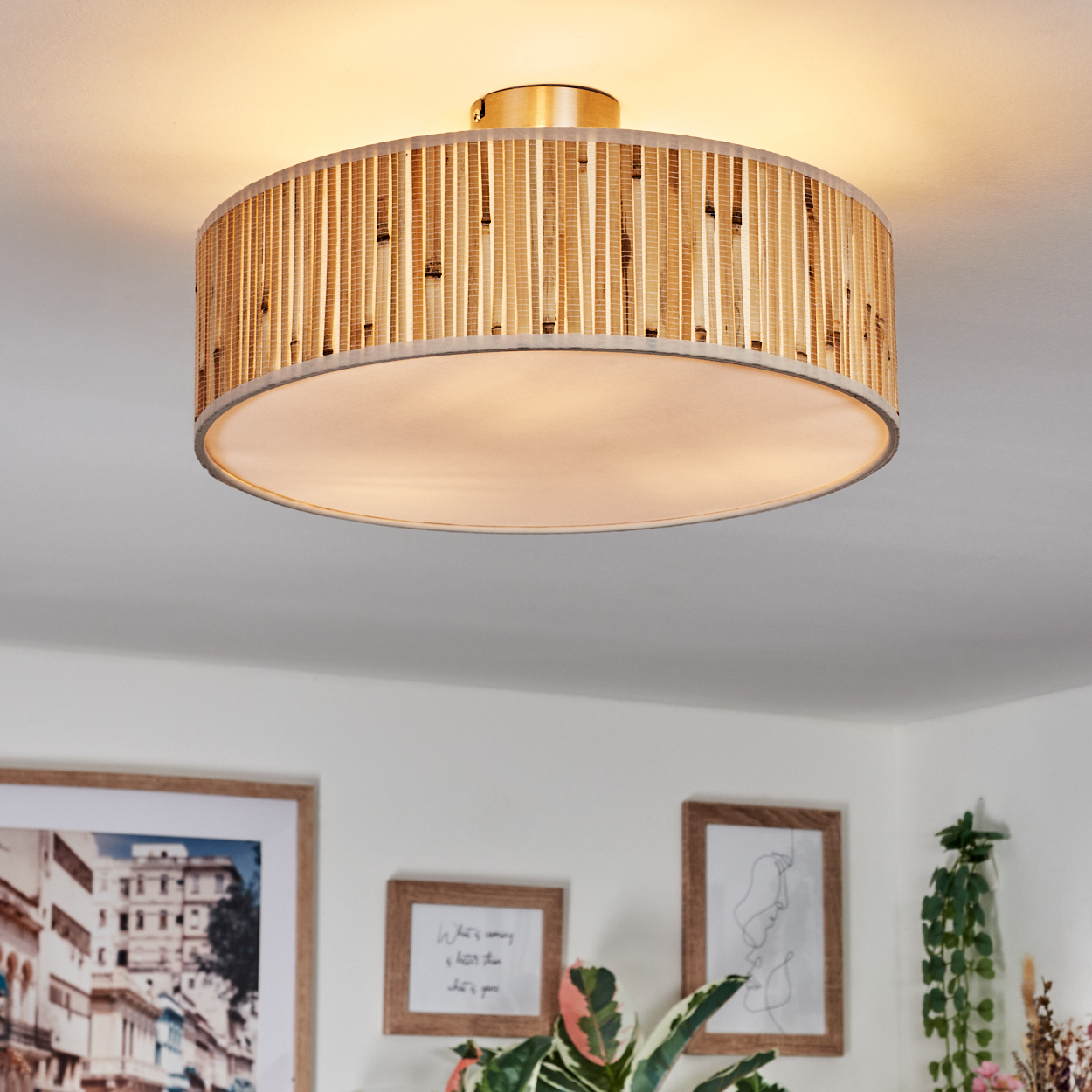 Eine Deckenlampe mit Bambusschatten ist an der Decke montiert. Darunter dekorieren gerahmte Bilder und Pflanzen den Raum.