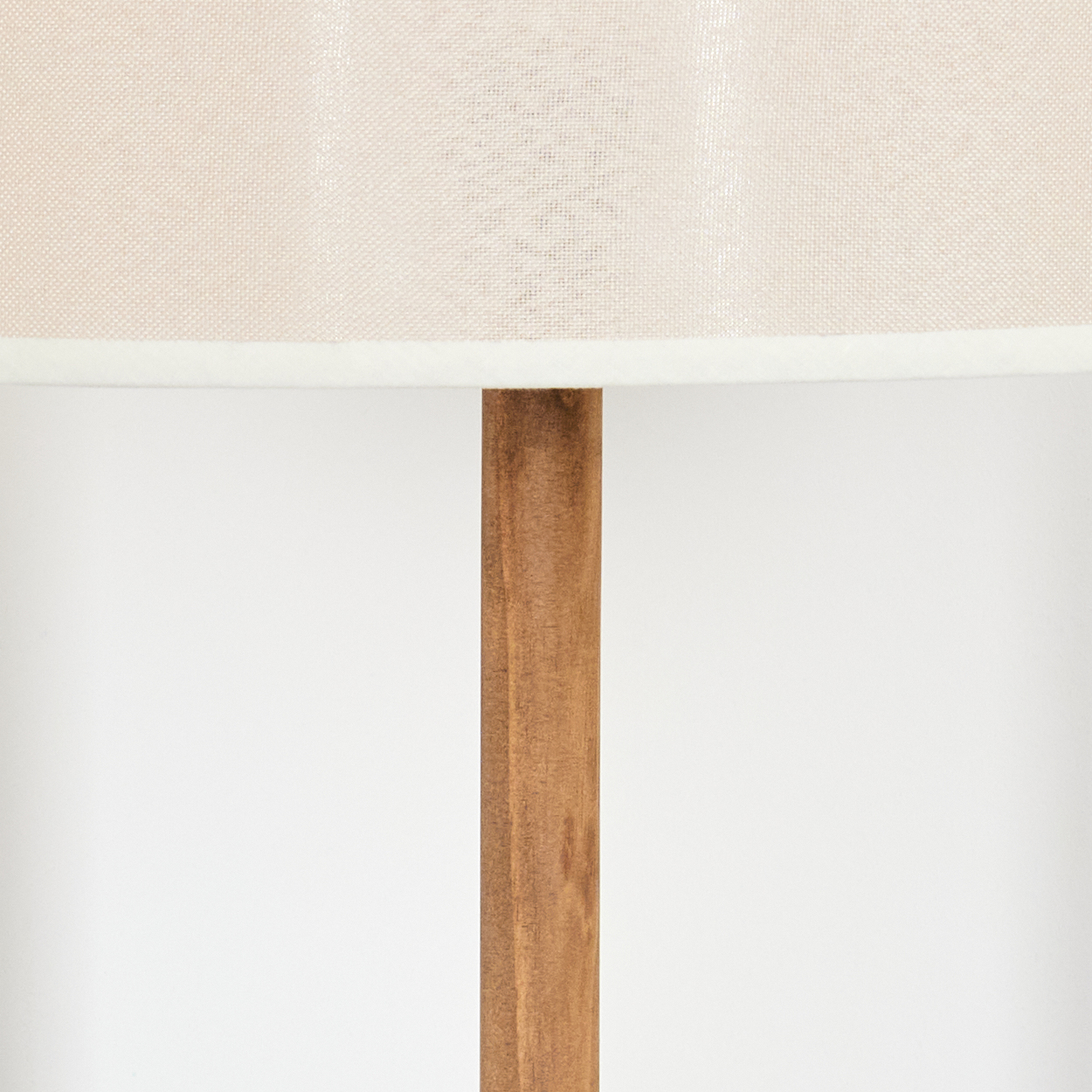 Nahaufnahme einer Lampe. Beiger Lampenschirm mit weißem Rand sitzt auf einem braunen Holzpfosten auf weißem Hintergrund.