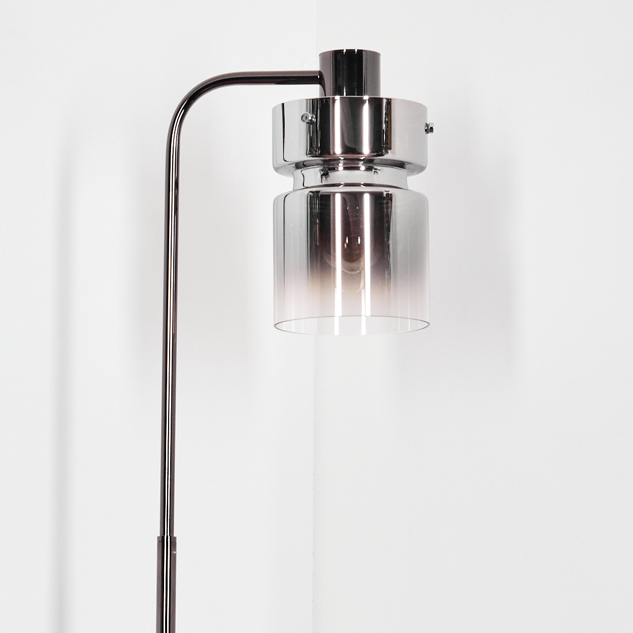 Eine moderne Stehlampe mit Chrom- und Glasschirm. Der Schirm hat einen Farbverlauf, und die Lampe steht vor einer weißen Wand.