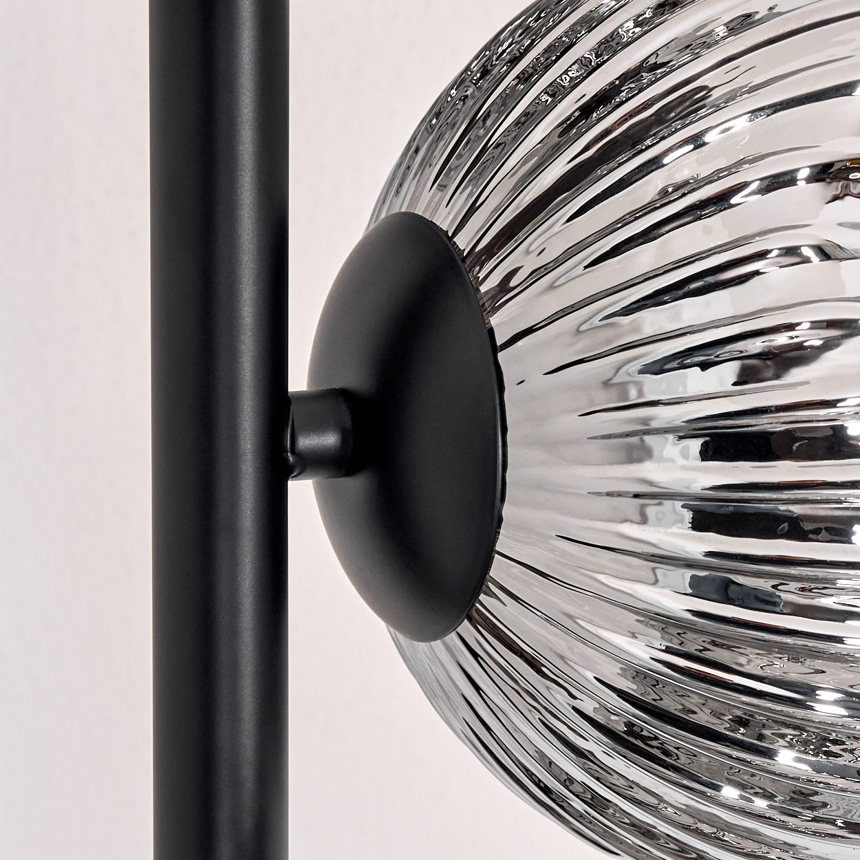 Nahaufnahme einer modernen Lampe. Sie hat einen schwarzen Metallmast und einen kugelförmigen, geriffelten Glasschirm. Der Hintergrund ist weiß.