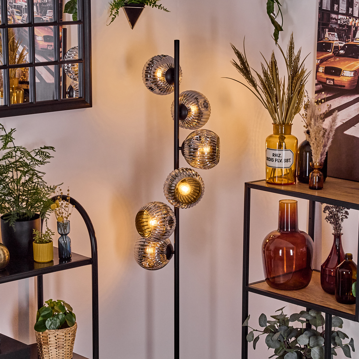 Eine moderne Stehlampe mit Glaskugelschirmen, umgeben von Regalen mit Pflanzen und dekorativen Vasen, vor einer Wand.
