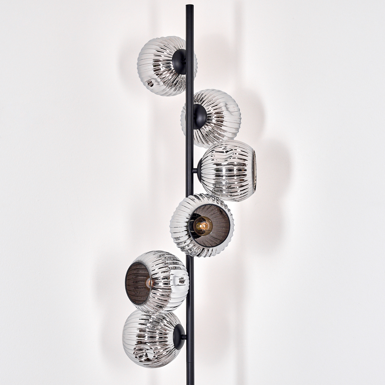 Eine moderne Lampe mit sechs silbernen, geriffelten Glaskugeln an einer schwarzen Metallstange. Eine einzelne Glühbirne leuchtet.