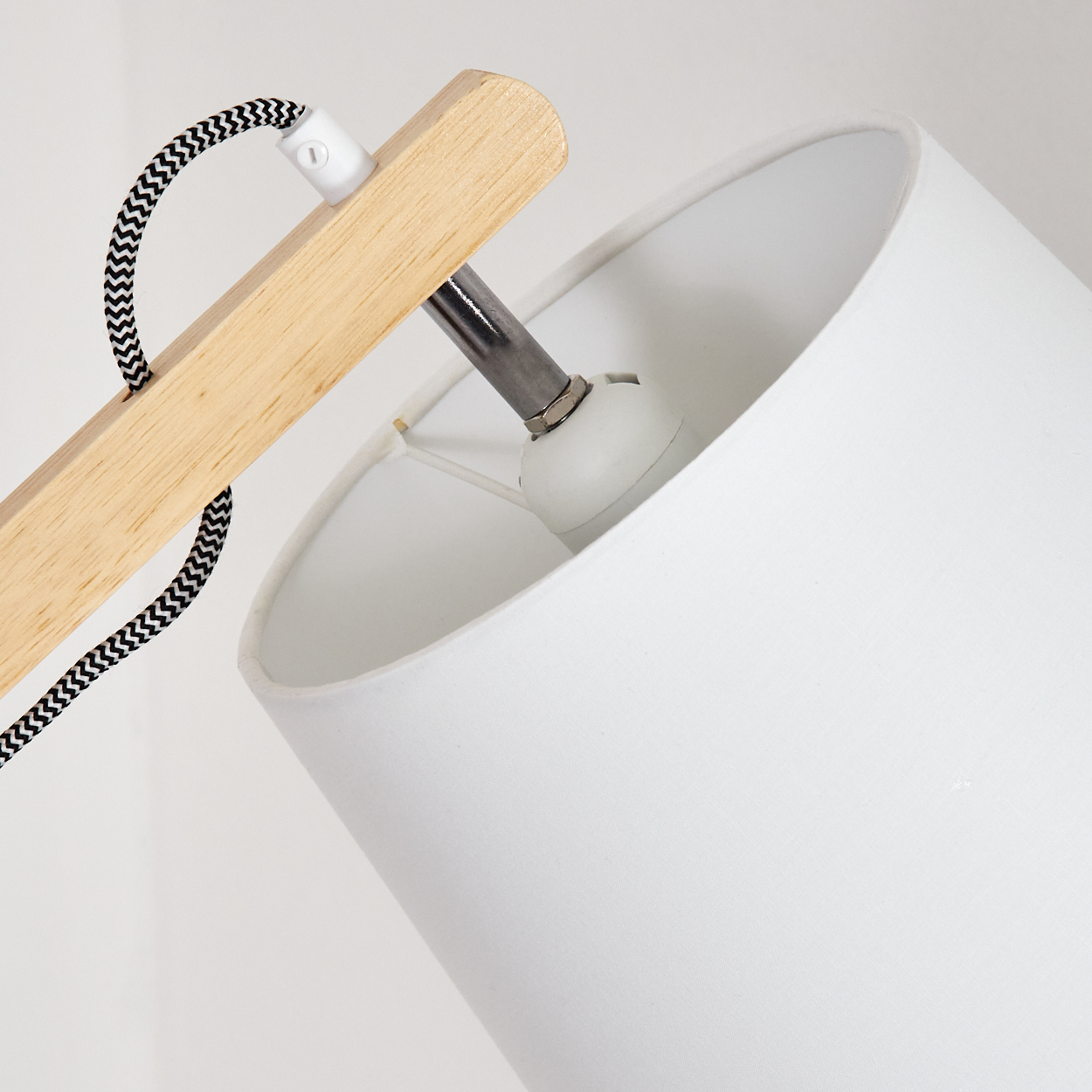 Nahaufnahme einer weißen Lampe. Sie hat einen Holzarm, einen weißen Lampenschirm und ein schwarz-weiß gestreiftes Kabel.