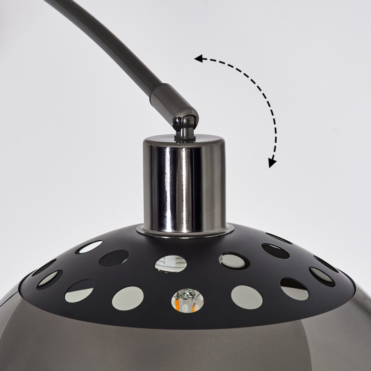 Nahaufnahme einer Lampe. Schwarzer Schirm mit Löchern, Chromfuß und gebogenem Arm. Ein Pfeil zeigt, dass die Lampe verstellbar ist.