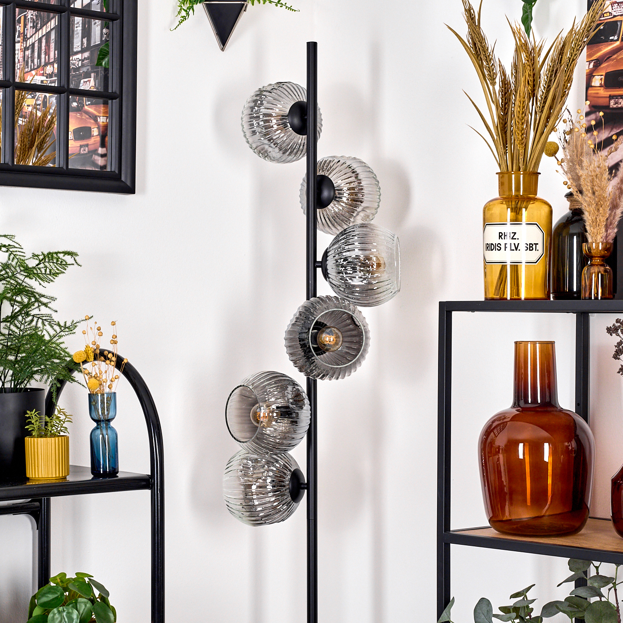 Eine moderne Stehlampe mit Glasschirmen, neben Regalen mit Vasen und Pflanzen. Ein gerahmtes Bild hängt an der Wand.