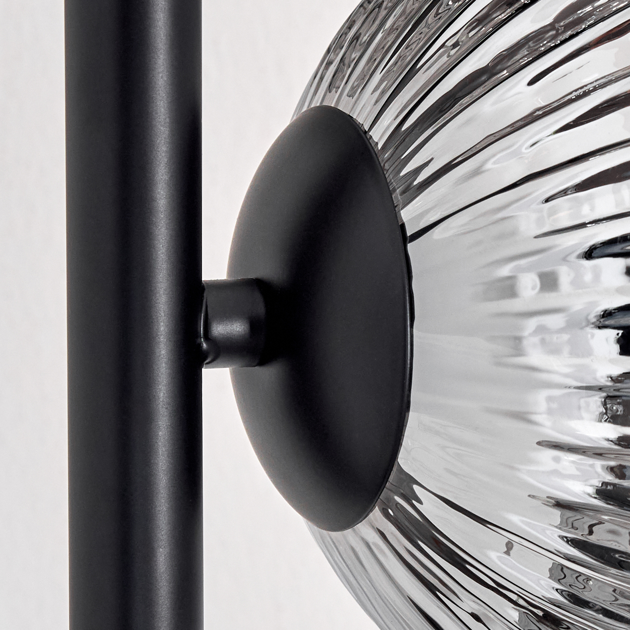 Nahaufnahme einer schwarzen Lampe. Eine schwarze Stange verbindet sich mit einem runden schwarzen Teil, das einen geriffelten Glasschirm hält.