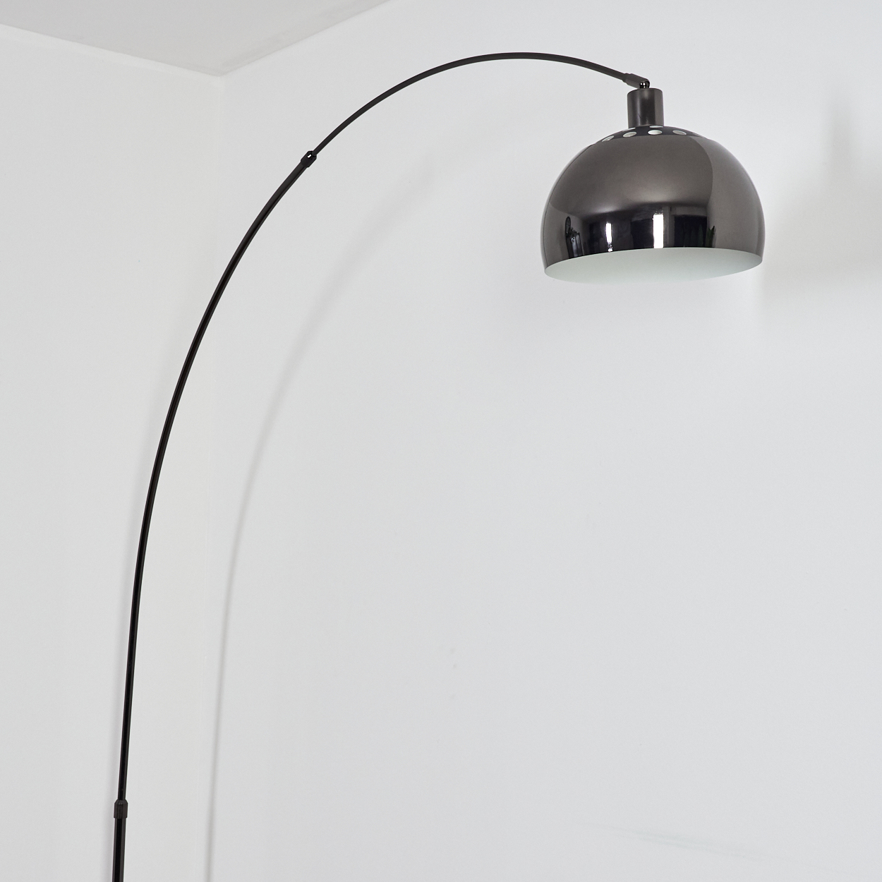 Eine moderne, schwarze Bogen-Stehlampe mit einem metallgrauen Lampenschirm steht vor einer weißen Wand.