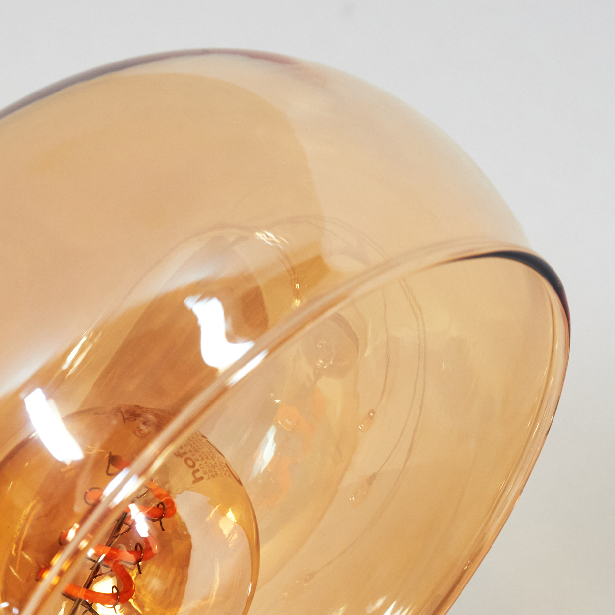 Nahaufnahme eines orange-gelben Glasschirmes. Eine Glühbirne ist sichtbar. Der Hintergrund ist weiß.
