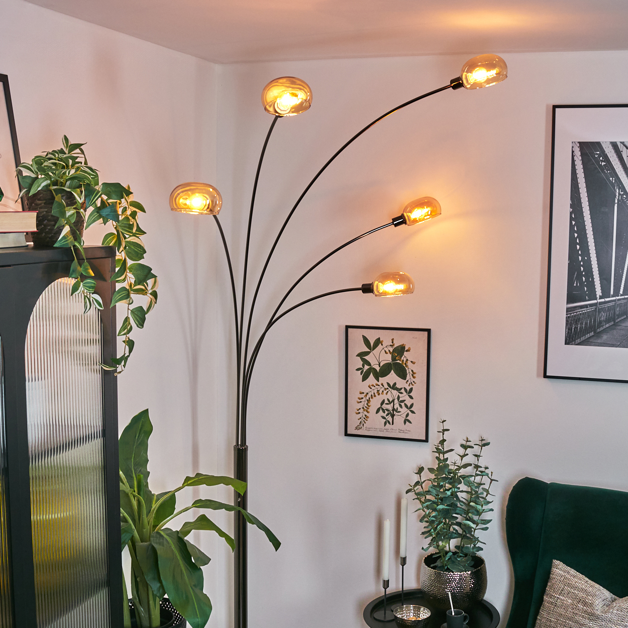Ein modernes Wohnzimmer mit einer schwarzen Stehlampe mit fünf Glühbirnen. Pflanzen und Kunst sind ebenfalls zu sehen, darunter ein grüner Sessel.