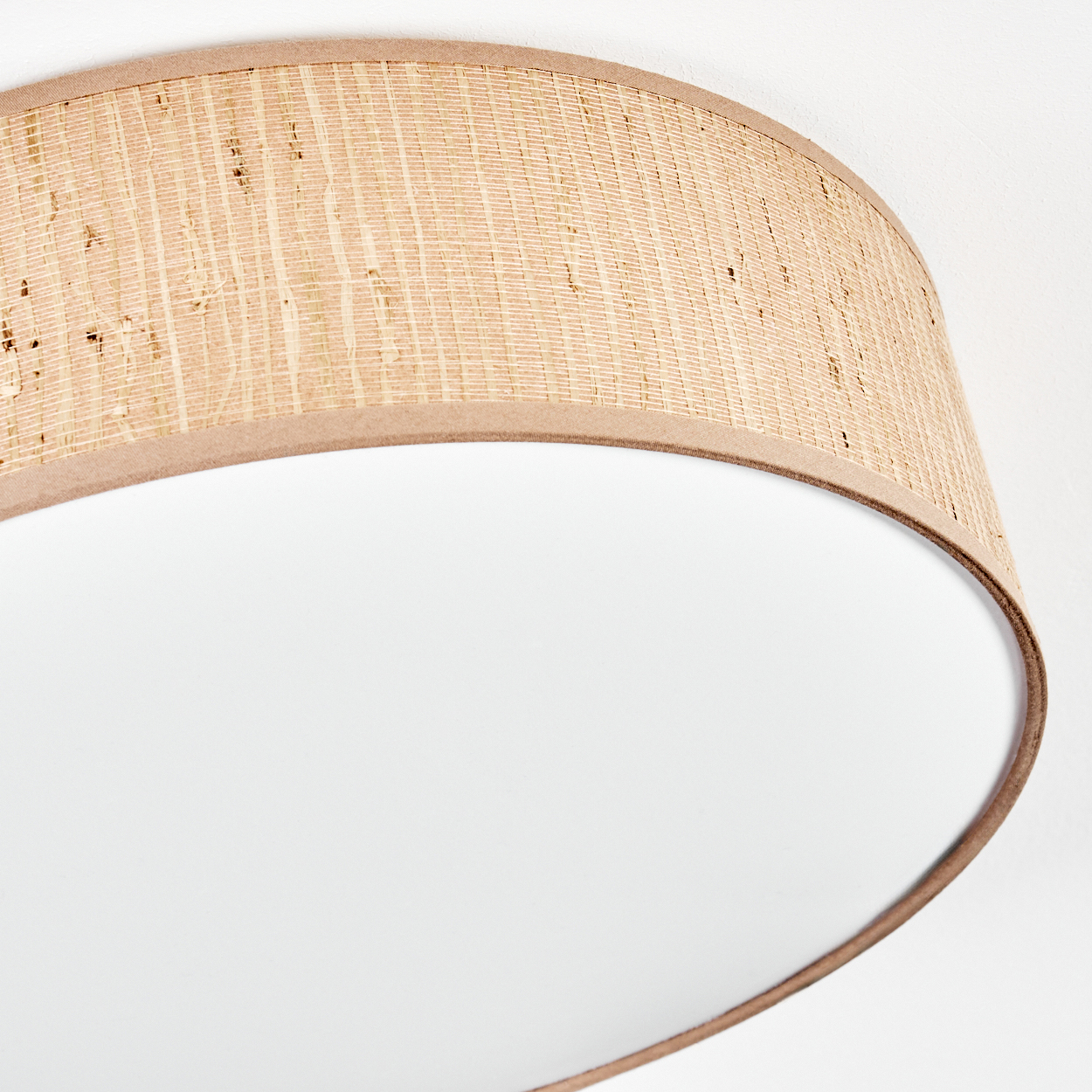 Nahaufnahme einer Lampe. Die Lampe hat einen hellbraunen, gewebten Schirm mit dunkler brauner Einfassung und weißem Innenraum.