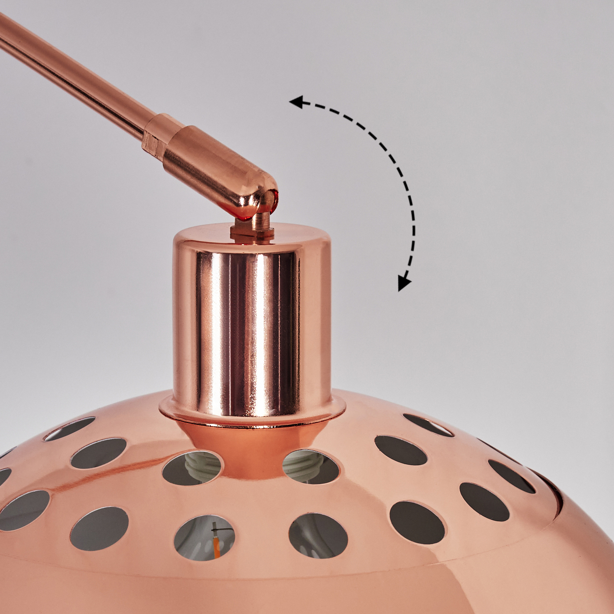 Detail einer kupferfarbenen Lampe. Ein gepunkteter Pfeil zeigt die Einstellung an. Die Lampe hat einen perforierten Schirm.