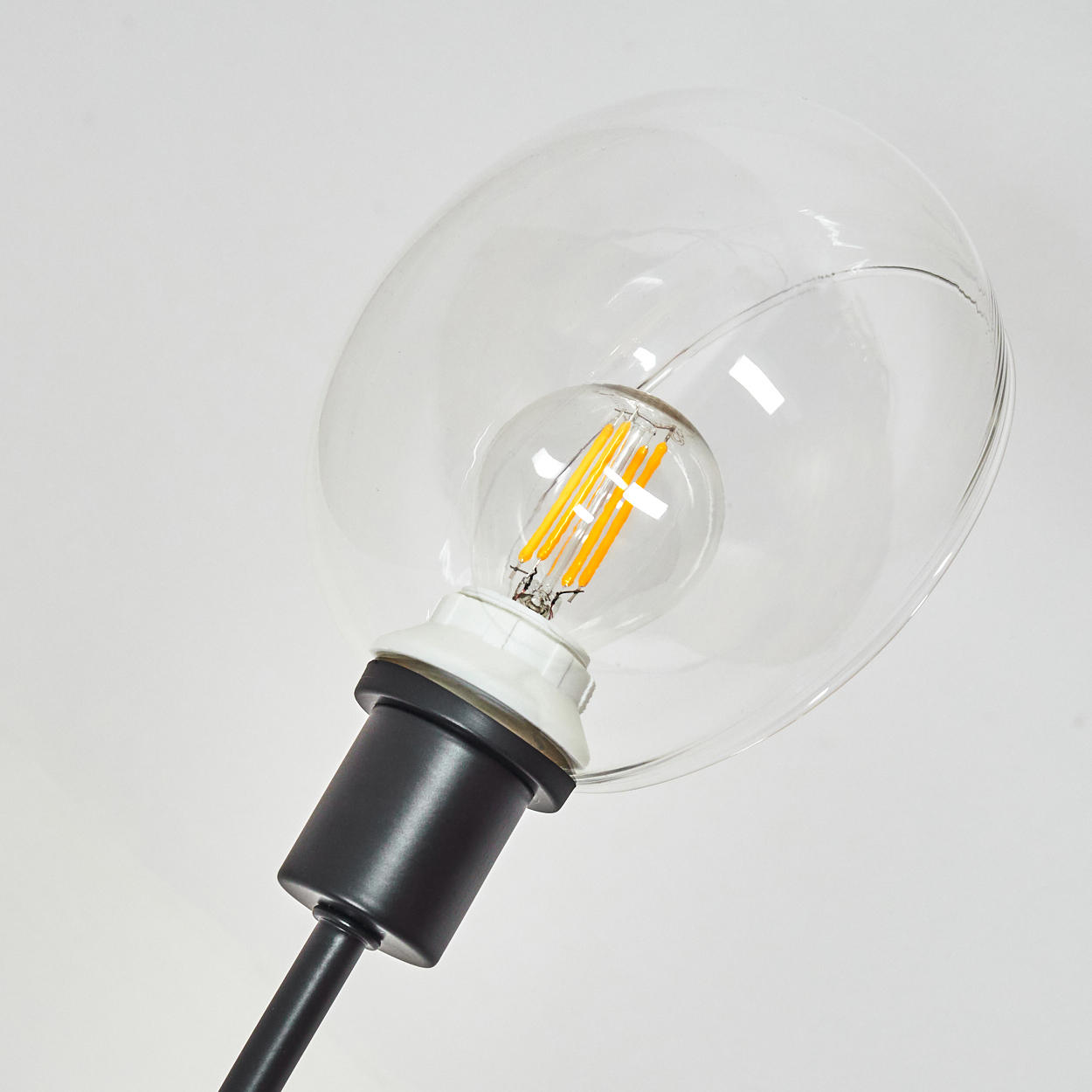 Nahaufnahme einer modernen Lampe. Eine transparente Glühbirne umschließt eine Glühbirne mit gelben Filamenten, montiert auf einem schwarzen Stiel.