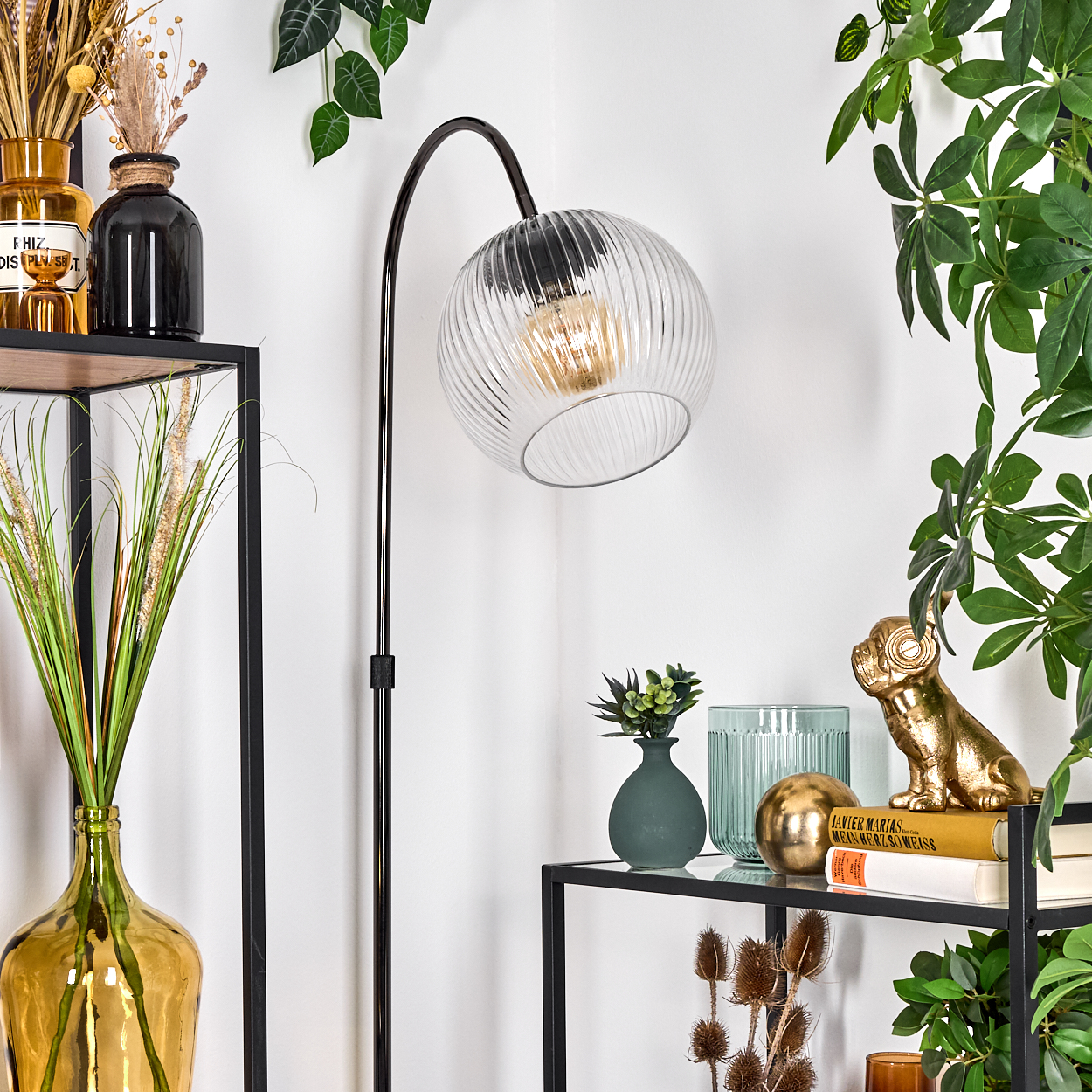 Ein modernes Interieur mit Stehlampe und Regalen. Die Regale beherbergen Vasen, Pflanzen, Bücher und eine goldene Hundestatue.