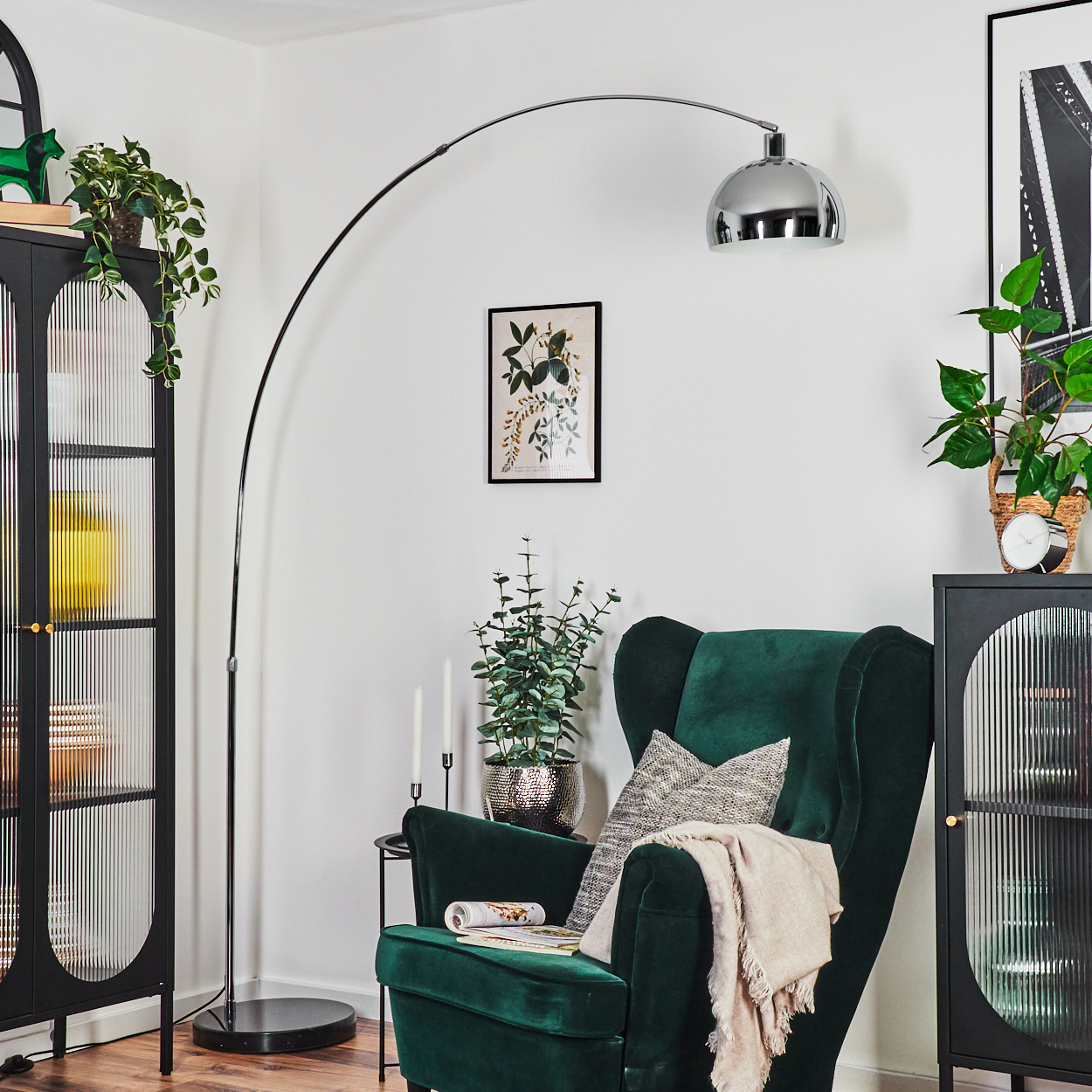 Ein grüner Sessel mit einer Decke steht unter einer Bogenlampe. Pflanzen und Dekoration sind im Hintergrund.