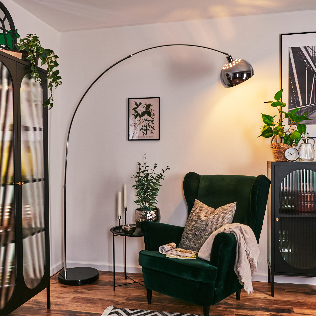 Wohnzimmerszene mit grünem Sessel, Stehlampe, schwarzem Schrank und Pflanzen. Ein Teppich, ein kleiner Tisch und dekorative Gegenstände sind vorhanden.