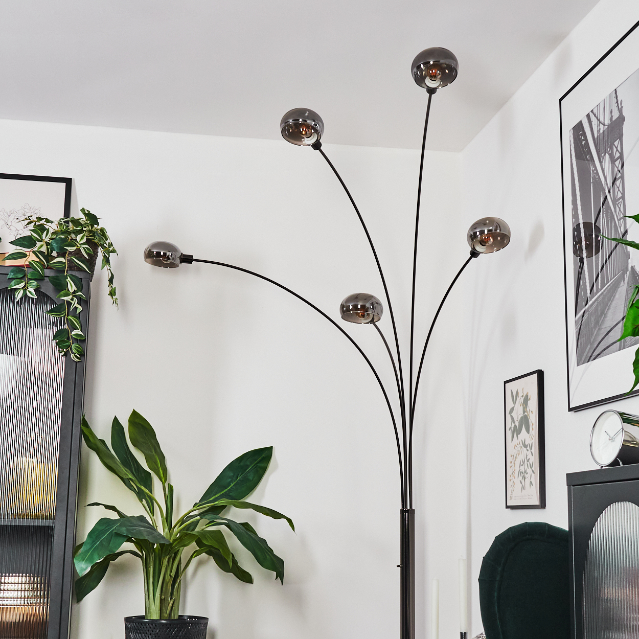 Ein modernes Wohnzimmer mit einer schwarzen Stehlampe mit fünf kugelförmigen Lichtern, Pflanzen und gerahmten Kunstwerken.