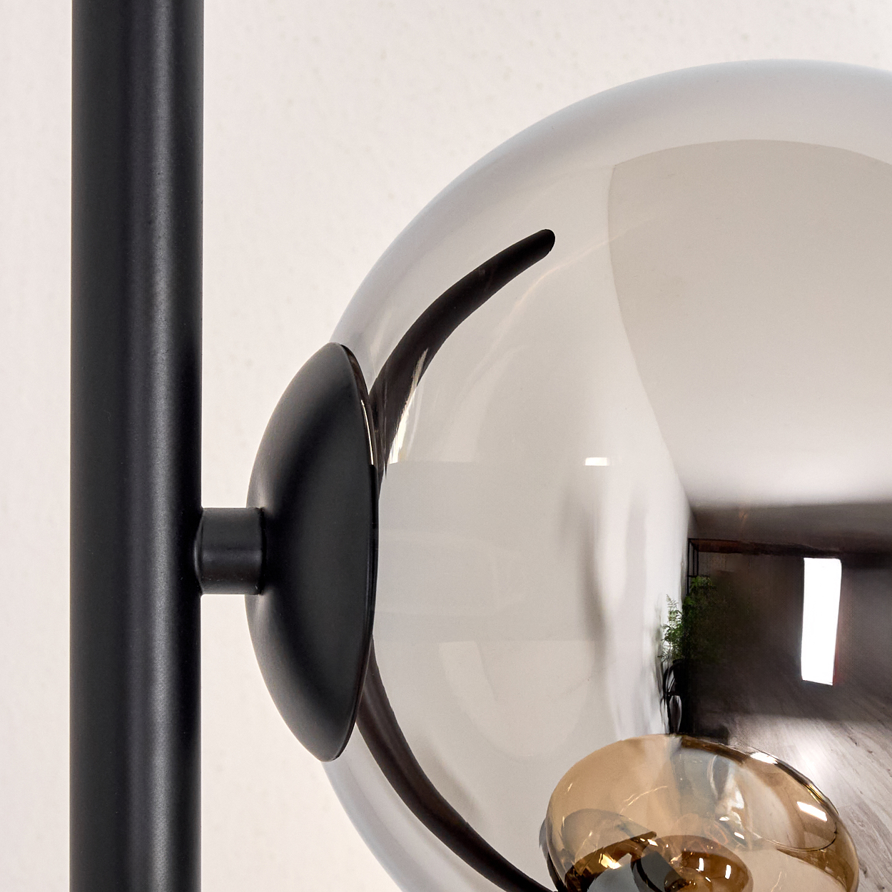 Nahaufnahme einer schwarzen Metalllampe. Eine große, transparente Kugel reflektiert einen Raum. Darunter ist ein kleineres, bernsteinfarbenes Licht sichtbar.